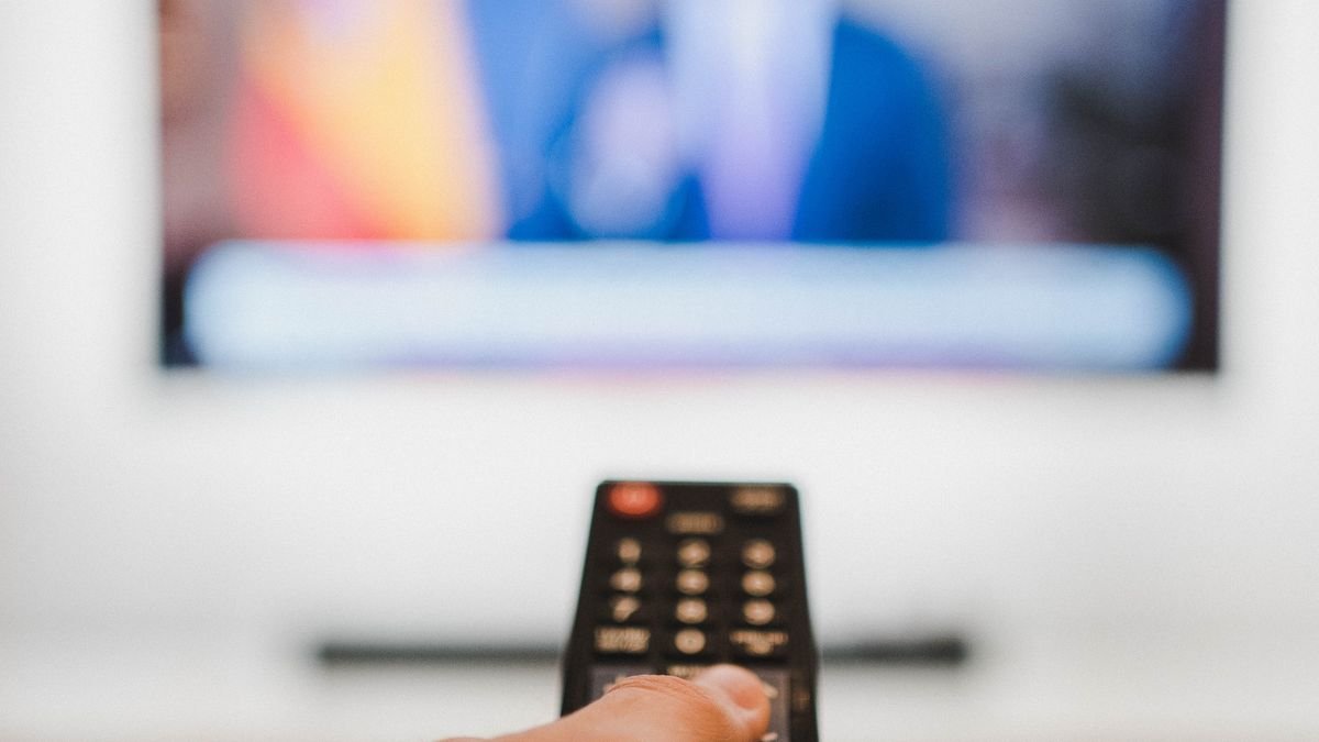 Hand, die eine Fernbedienung auf einen Fernseher richtet